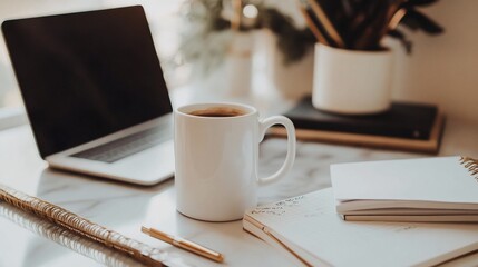 Work from home setting with a laptop, a white mug of coffee and a notebook with a gold pen