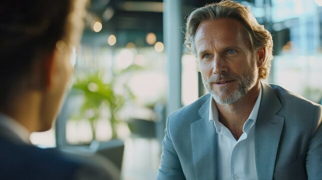 A businessman in a modern office, having a conversation with his team, while a digital presentation is displayed on a screen