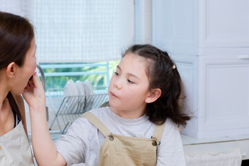 Asian mother and daughter sitting at kitchen table eating grapes together, enjoying happy snack time at home. Includes girl, mother, food, eating, family, kitchen, home, bonding, parenting, caring.