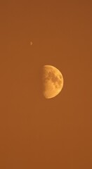 Stunning Celestial View: Half Moon and Distant Star in a Warm Orange Sky at Dusk