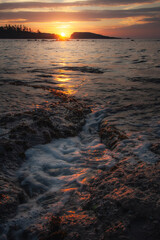Sunset over the ocean with glowing waves and rocky shoreline
