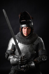 Portrait of a knight in full plate armor holding a sword posing isolated on a dark background