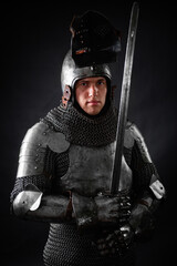 Portrait of a knight in full plate armor holding a sword posing isolated on a dark background