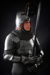 Portrait of a knight in full plate armor holding a sword posing isolated on a dark background