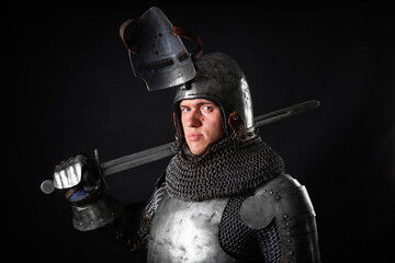 Portrait of a knight in full plate armor holding a sword posing isolated on a dark background