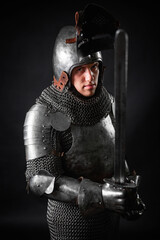 Portrait of a knight in full plate armor holding a sword posing isolated on a dark background