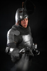Portrait of a knight in full plate armor holding a sword posing isolated on a dark background
