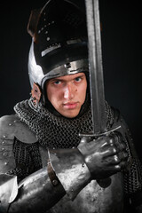 Portrait of a knight in full plate armor holding a sword posing isolated on a dark background