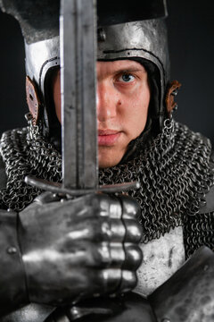 Portrait of a knight in full plate armor holding a sword posing isolated on a dark background