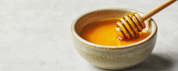 Bowl of honey with a honey dipper on a textured surface.