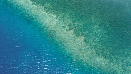 Aerial view of coral reef in clear tropical water, deep blue to turquoise gradient