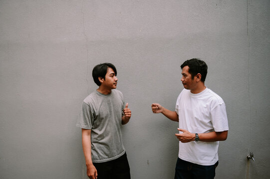 Two men facing each other in a casual conversation outdoors on plain background