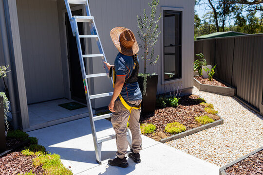 Electrician tradie man stabilising ladder to roof of small suburban house