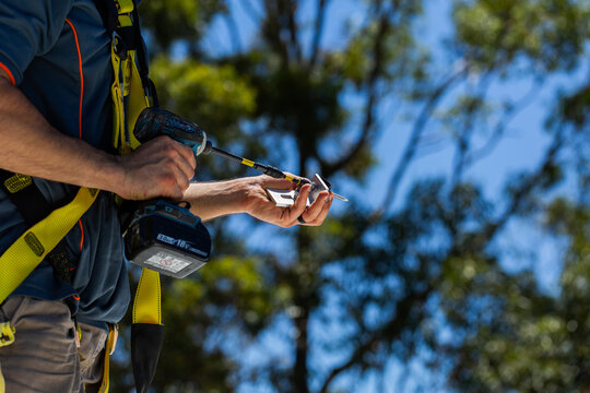 Electrician workman using drill to attach rails to roof for solar panel installation job