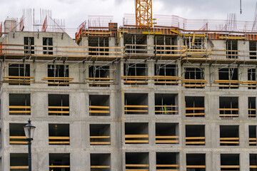 Fototapeta premium View of a multi-story building under construction, with visible window openings, formwork, and scaffolding. The concrete structure is in the raw state, and a portion of a tower crane is visible at the