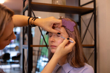 A makeup artist makes makeup for a young beautiful girl in a beauty salon.
