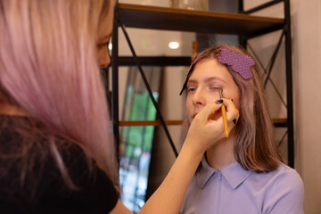 A makeup artist makes makeup for a young beautiful girl in a beauty salon.
