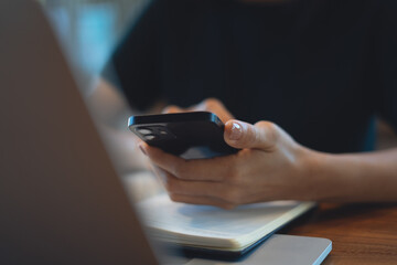 Closeup, business woman using mobile phone during remote working on laptop computer at coffee shop. Freelancer, entrepreneur using smartphone, online working. 