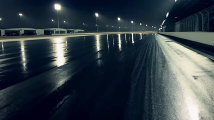 Dark asphalt race track with reflections under bright stadium floodlights and white garage buildings at night offers a cinematic feel - Powered by Adobe