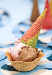 Balls of chocolate and raspberry ice cream in a waffle bowl decorated with a brightly colored waffle cone. Summer cooling dessert, Blue background