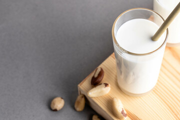Brazil nut milk is presented in a clear glass with a straw, placed on a wooden surface, surrounded by scattered nuts, creating a natural and inviting atmosphere for healthy living
