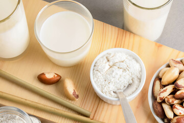 Brazil nut milk and powder are beautifully arranged on a wooden surface, showcasing their natural textures and colors, with additional nuts and glass containers enhancing the scene