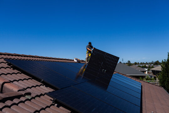 Aussie tradie man installing solar panels on hot sunlit roof of Australian home