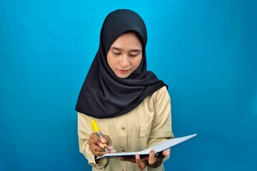 Young Muslim woman wearing hijab writing in notebook at study desk. Symbol of education, goal setting, journaling, and focus on personal growth.