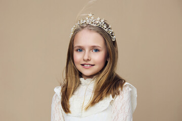 Charming young girl with a tiara and elegant dress, showcasing a joyful expression against a soft...