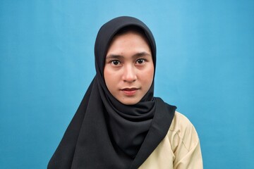 Young Muslim woman wearing a hijab applying makeup with a brush in front of a mirror. Concept of...