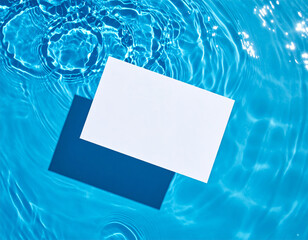 Piece of paper floats on pool surface, creating ripples and reflections in bright blue water, casting distinct shadow