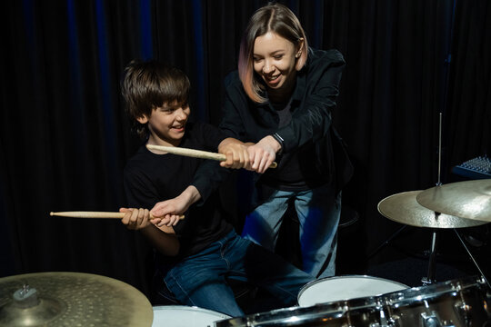 Young caucasian woman teaches a boy to play the drums in the studio on a black background. Music school student