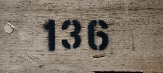 The number 136 is spray painted with black spray paint on wood