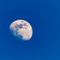 Detailed megazoom (600mm) view of the moon with craters during daytime with blue sky