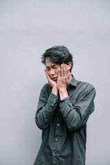 Man experiences intense pain holding face with hands against a wall