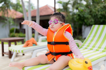 Cute little Asian girl in life jacket is preparing to play in swimming pool. Asian girl in life...