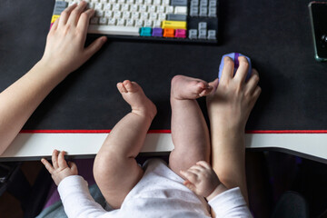 Parent balancing work and childcare, typing on keyboard with one hand while using a mouse with the other. A baby rests on their lap, illustrating modern multitasking.