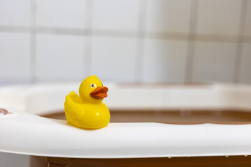 Yellow rubber duck placed on the edge of a white and brown bathtub, adding a playful touch to bath...
