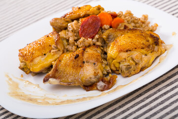 Delicious barley porridge with roasted chicken thighs and vegetables on white dish ..