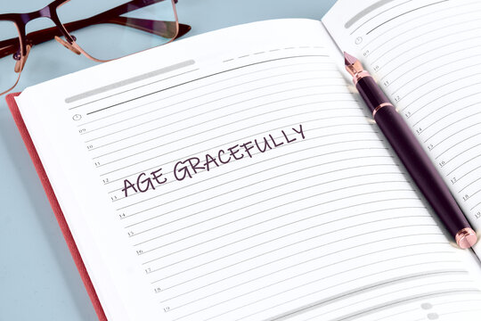 A well-organized journal lies open with the phrase age gracefully written boldly on the page. A stylish pen rests nearby, ready for notes. Glasses hint at contemplation and planning