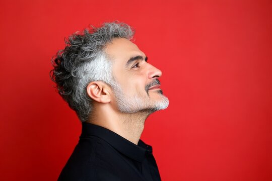 Red solid background. A sophisticated male posing with grace. Modish men's two-block cut haircut - midlife middle eastern man with curly hair. Creative of style for aging men.
