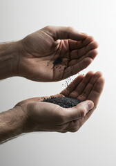 Hands gracefully pour a cascade of dark seeds against a clean, minimalist backdrop.