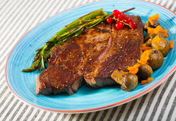 Roasted veal steak with seasonings served with baked vegetables and rosemary on striped textile surface