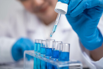 A scientist in gloves uses a pipette to add liquid to test tubes filled with blue solutions in a laboratory setting.