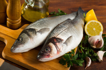 Raw European sea bass fish with ingredients on wooden table