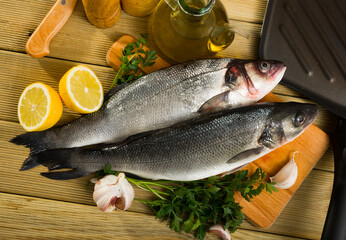 Cutting board with uncooked sea bass with lemon, garlic and greens