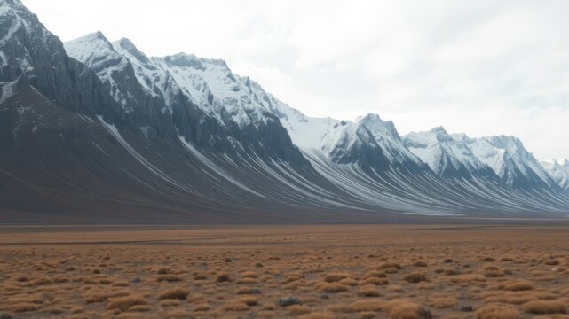 A breathtaking panoramic view of a majestic snow-capped mountain range stretches across a vast, desolate plain under a cloudy sky.