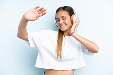 Fototapeta premium Young caucasian woman isolated on blue background listening music and dancing