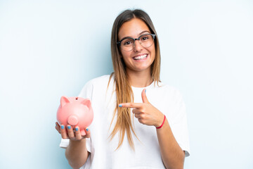 Young caucasian woman holding a piggybank isolated on blue background and pointing it