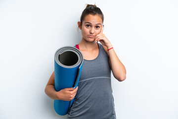 Young sport woman going to yoga classes while holding a mat isolated on white background thinking...